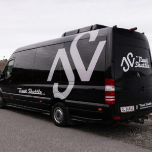 Black shuttle van parked beside a coastal road with water in the background