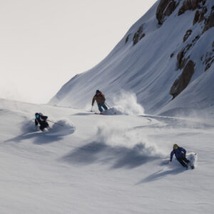 Three skiers carving through deep powder on a steep mountain slope